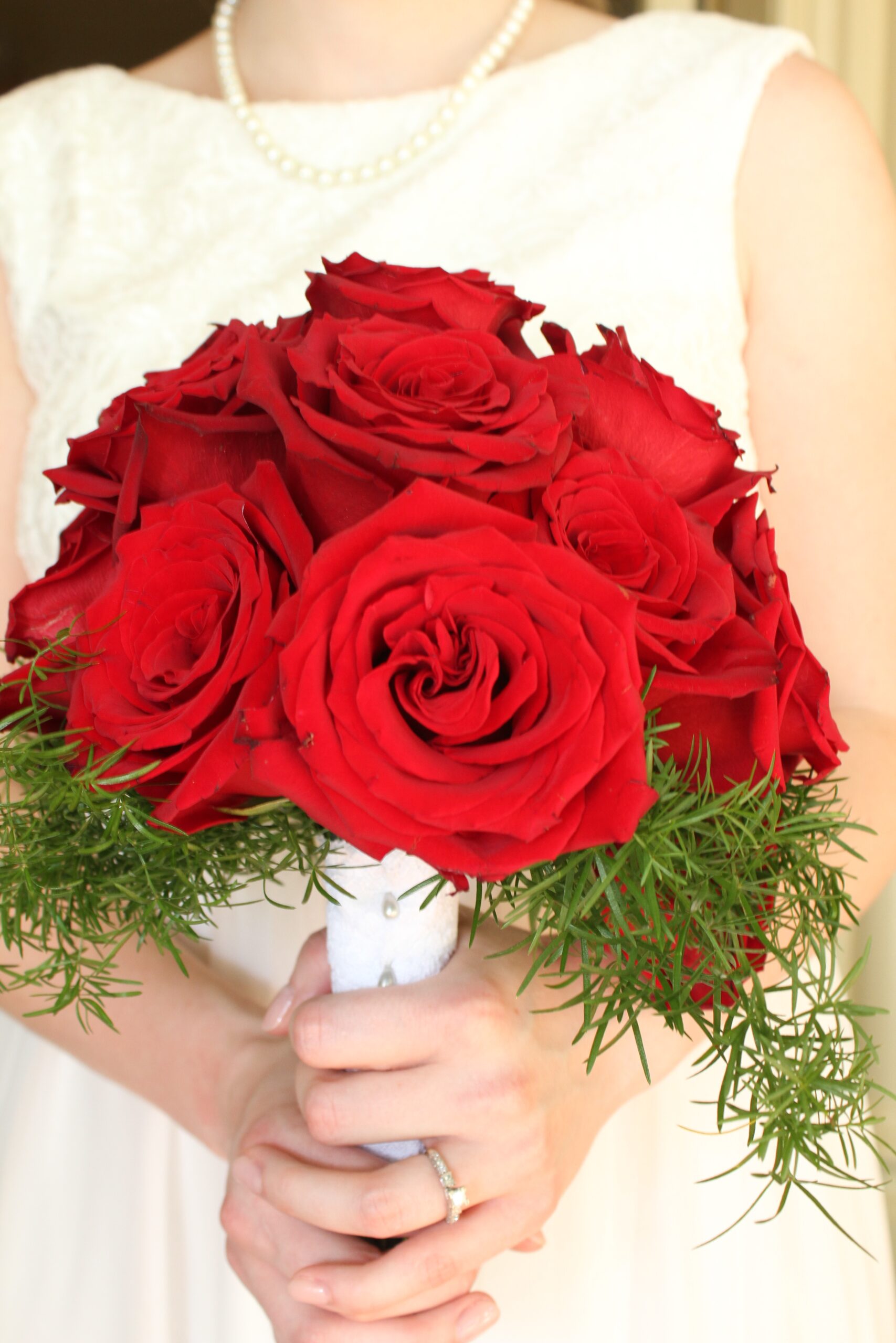 The bride, wearing a white lace sundress holds a large bouquet of red roses. 