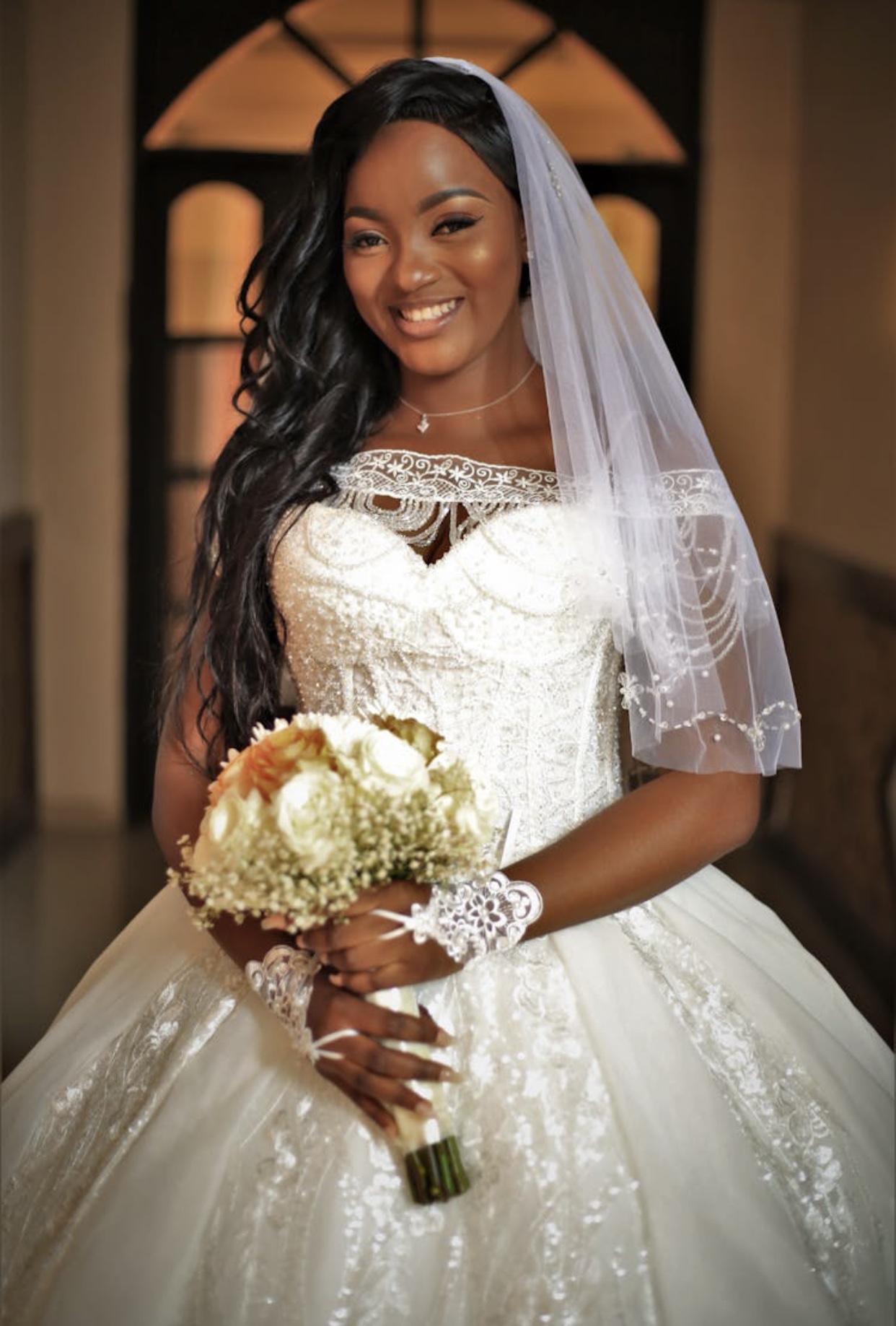 African American bride in an ivory wedding dress with a heavily beaded bodice and tulle skirt with an elbow length tulle veil. 