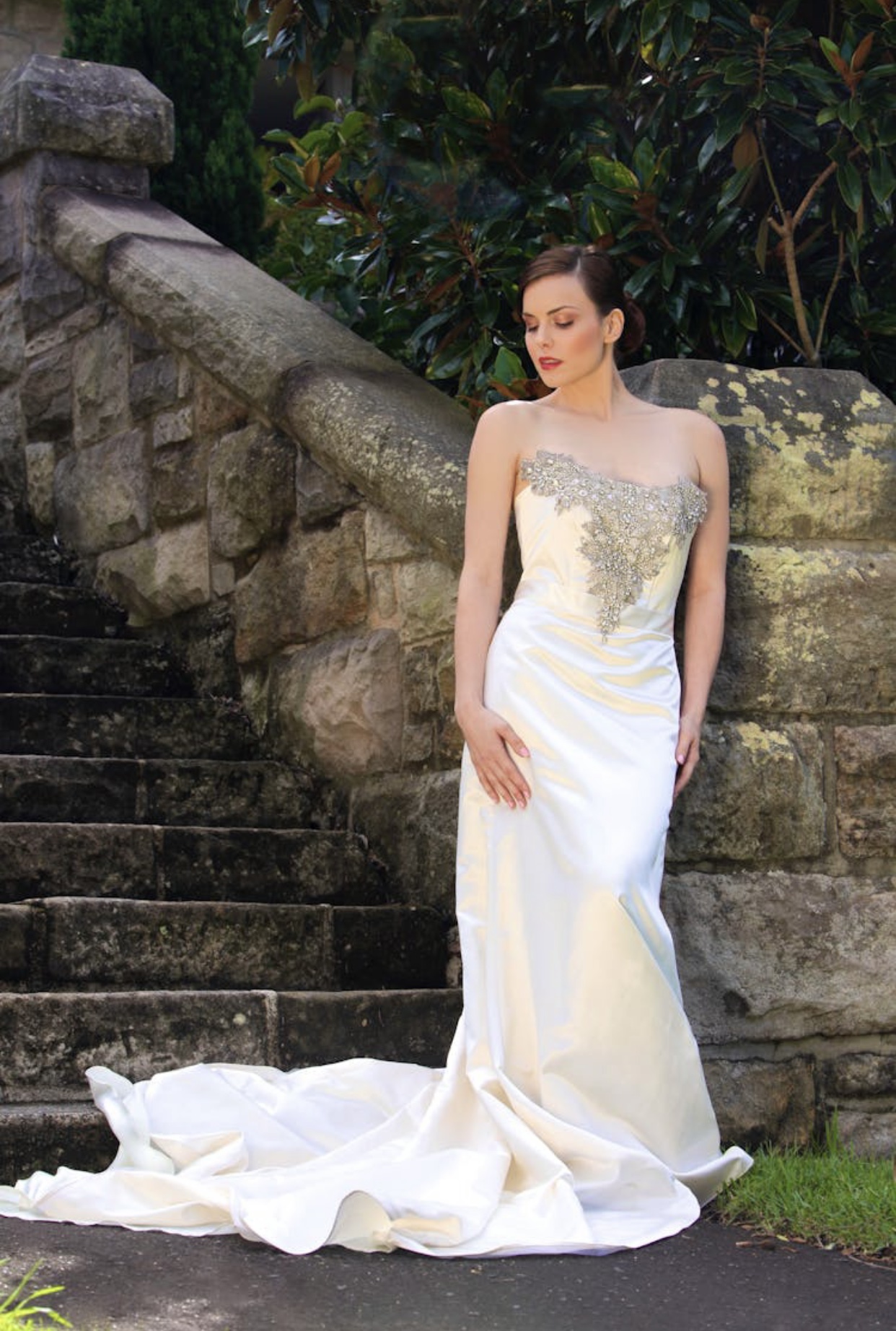 Dark haired bride in a fitted white sating wedding dress with long train and elaborately beaded bodice.