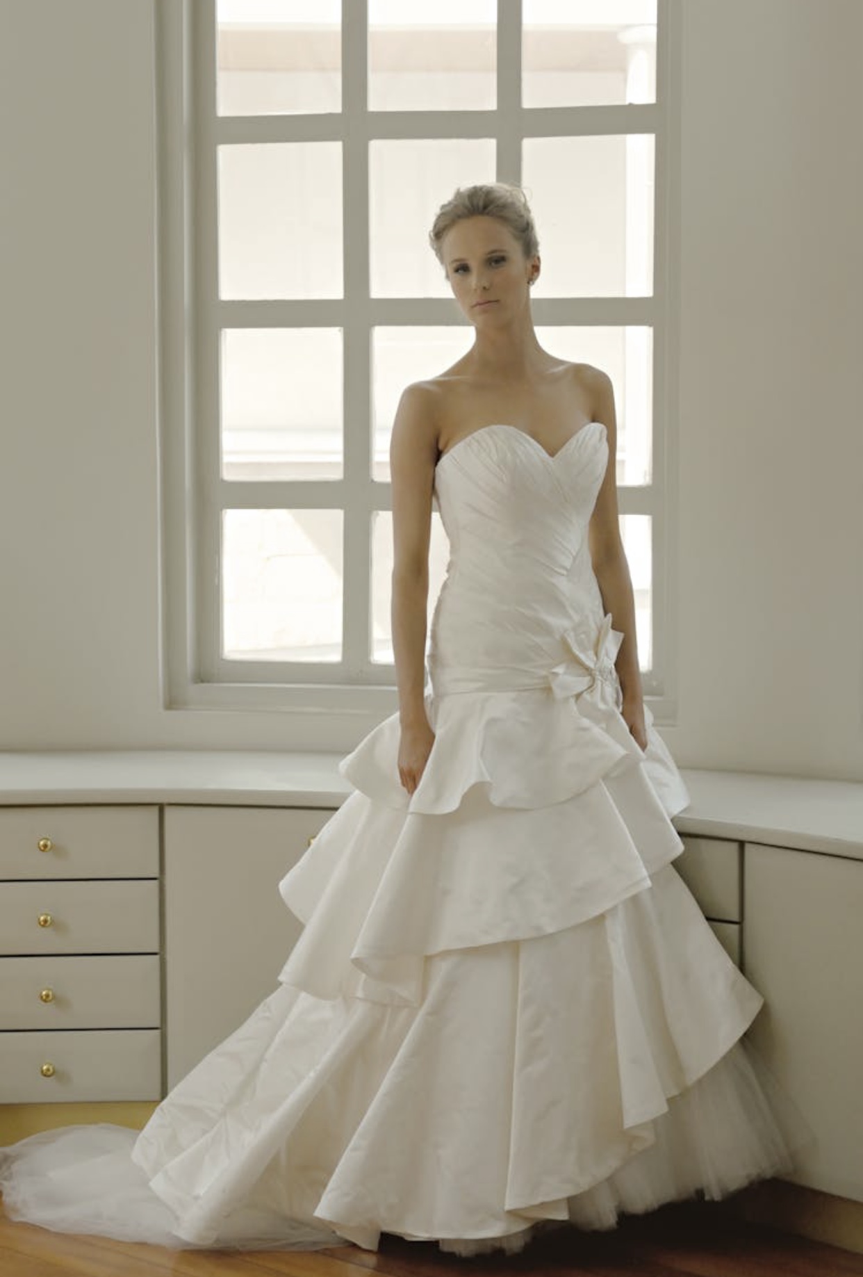 Blonde bride in a white satin trumpet wedding dress with a ruffled layered skirt and strapless sweetheart bodice. 