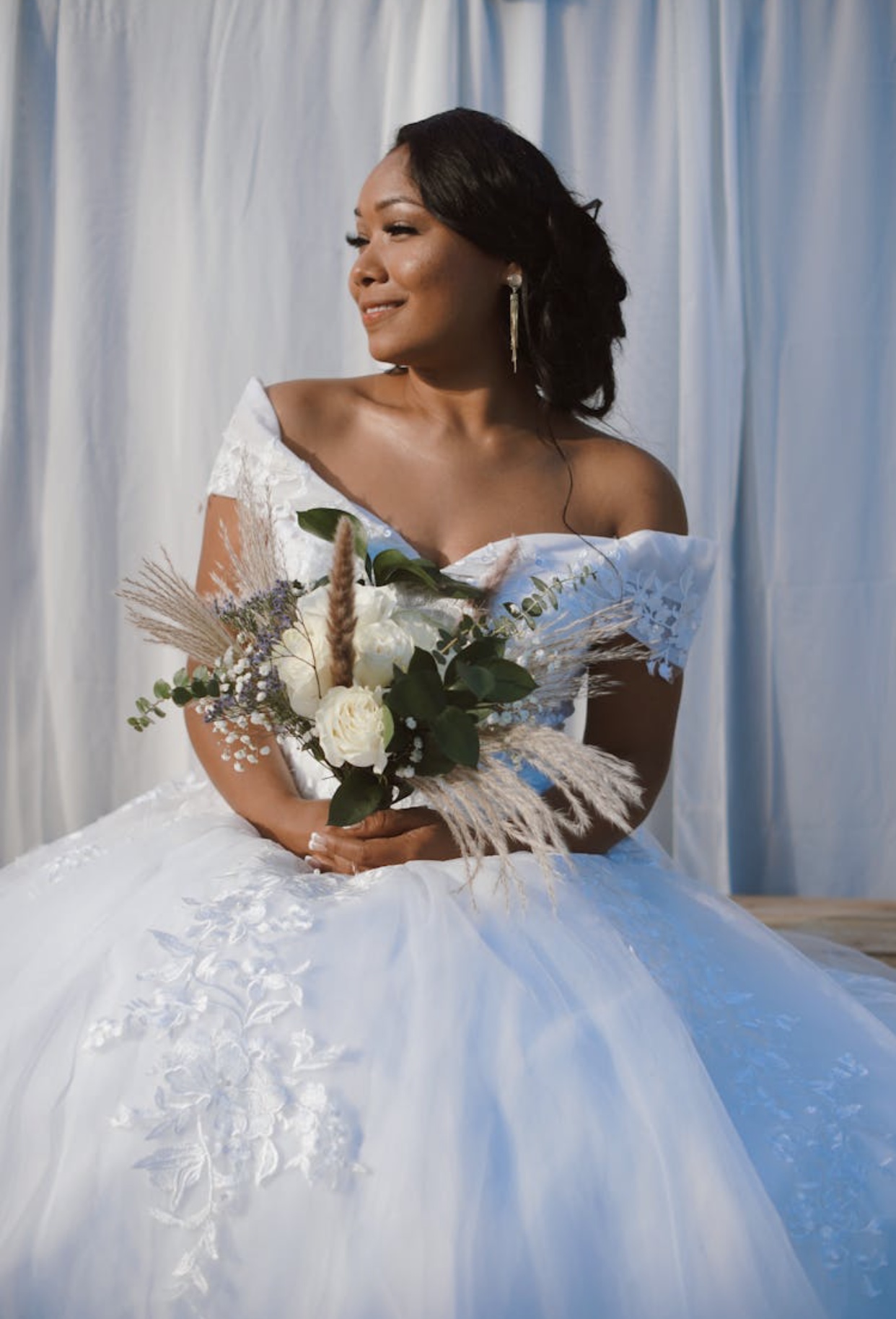 African American bride in an off the shoulder white lace wedding dress with a full tulle skirt accented by applique.