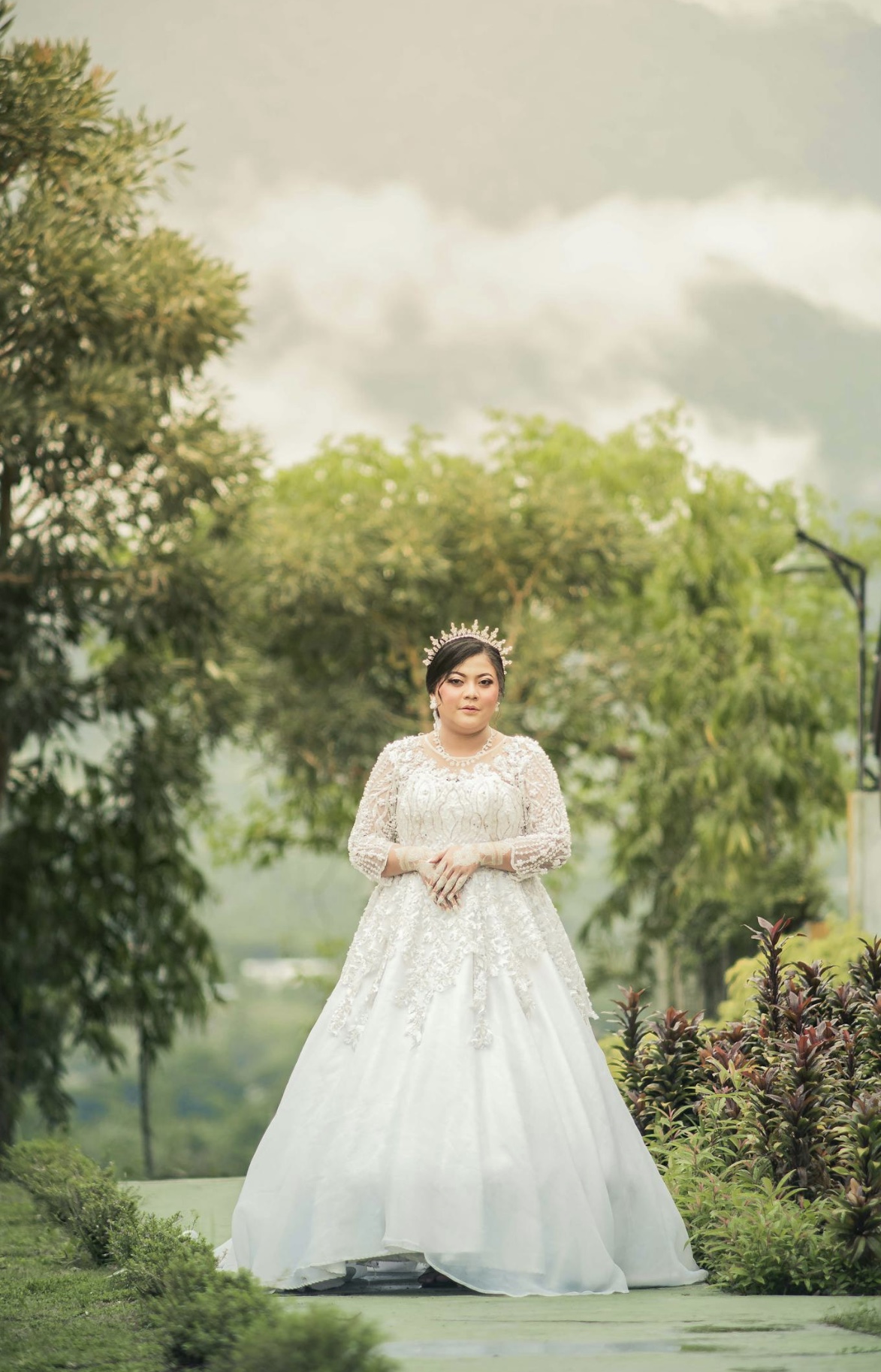 Hispanic bride in a sheer white long sleeve beaded overlay wedding gown with a full skirt and sunburst crown.