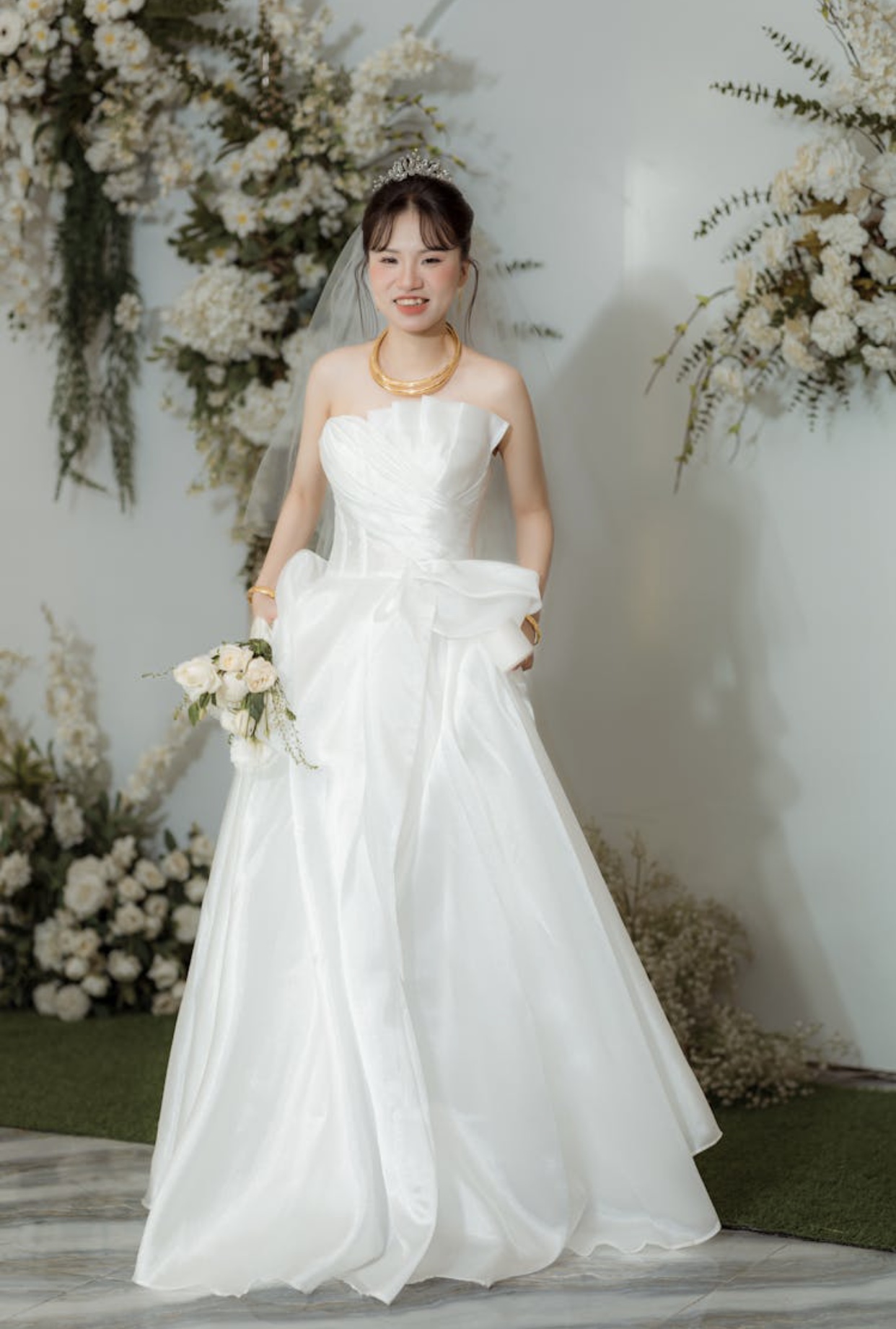 Asian bride in a flowing white satin wedding gown with an asymmetrical bodice and neckline. 