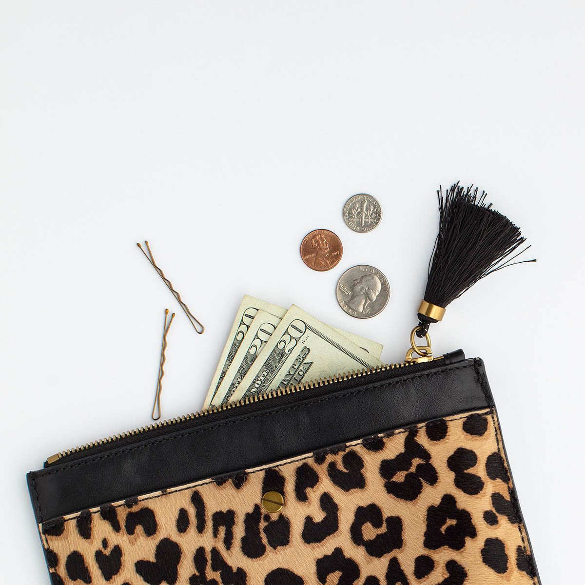 Leopard print wallet with a tassel on the zipper is open lying on the counter with three twenty dollar bills, a dime, penny and quarter and two bobby pins spilling out. 