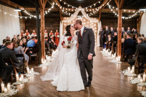 Bride and groom kissing during wedding underneath string lighting at Houston Station, Nashville wedding venue