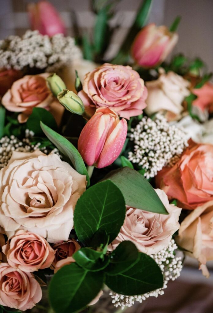 A detail image of a large floral arrangement containing greenery, blush, pink and peach roses, tulips, and rice flower.