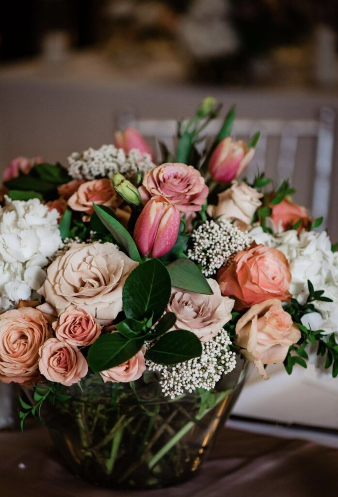 A detail image of a large floral arrangement containing greenery, blush, pink and peach roses, tulips hydrangea, rice flower, and ranunculus.