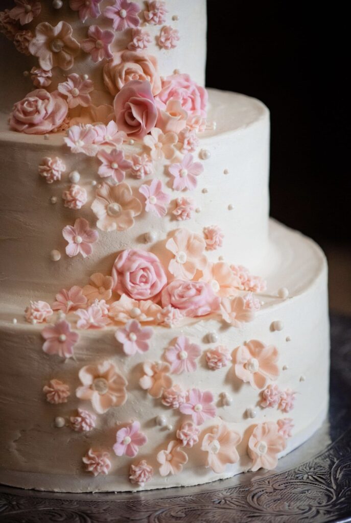 Detail of the lower half of a three tier wedding cake with ivory icing. The cake has peach, pink and blush sugar flowers cascading down the front. 