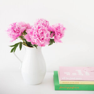 Pink peonies in a vase next to a stack of books