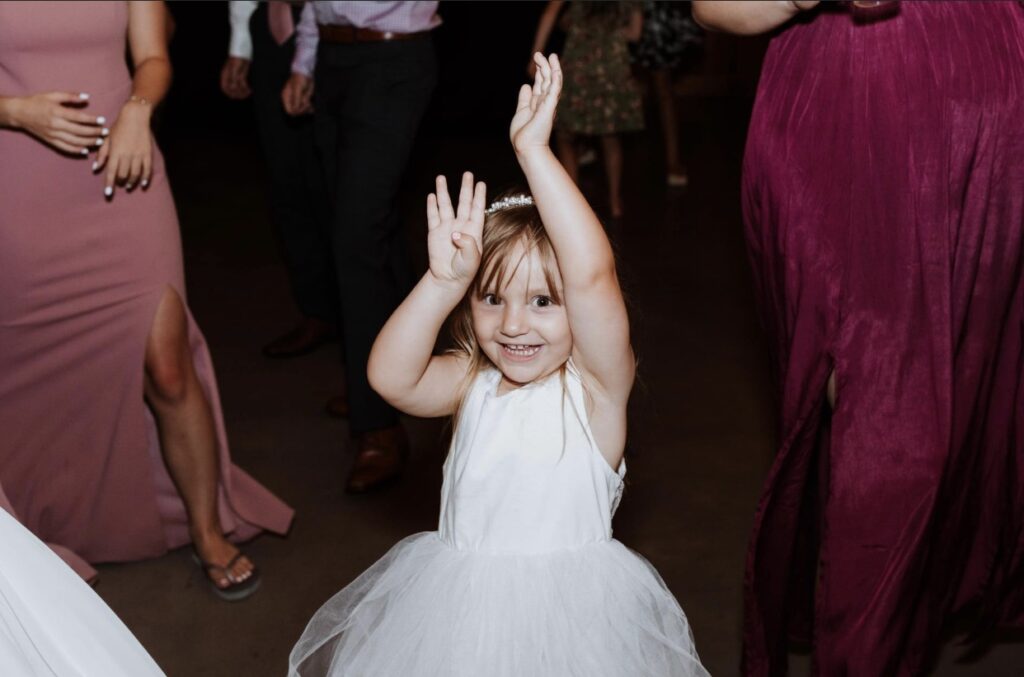 The flower girl dancing at a summer wedding at Steel Magnolia Barn