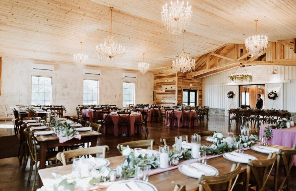 Steel Magnolia Barn is elegantly decorated for a summer wedding. The crystal chandeliers and cedar wood walls are set off with tables with rose linens and farm tables dressed with candles and greenery.