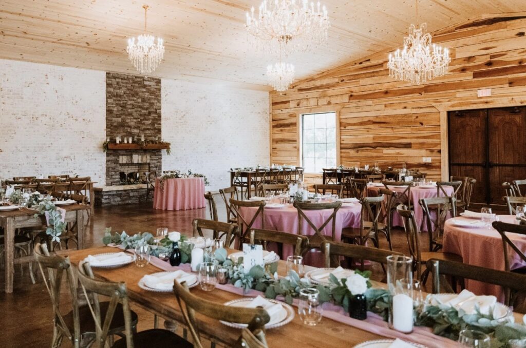 Steel Magnolia Barn is elegantly decorated for a rose and navy summer wedding. The crystal chandeliers and cedar wood walls are set off by rose colored table cloths.  The stone fireplace is the backdrop of the bride and groom's rose colored sweetheart table. 