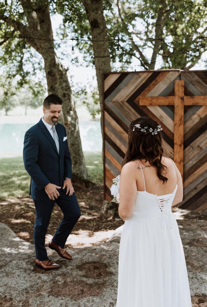 The bride's father sees her for the first time on her wedding day. They  stand on a limestone outcropping beside a striped wooden backdrop with a cross. 