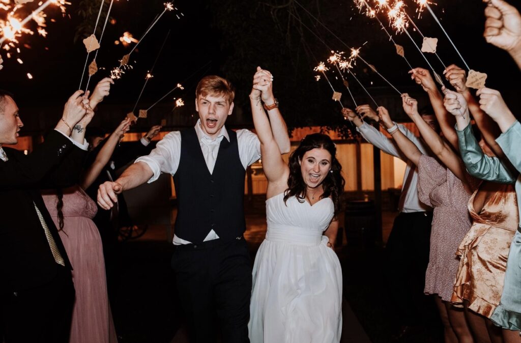 The bride and groom run through the sparkler send off with their hands held high in triumph. 