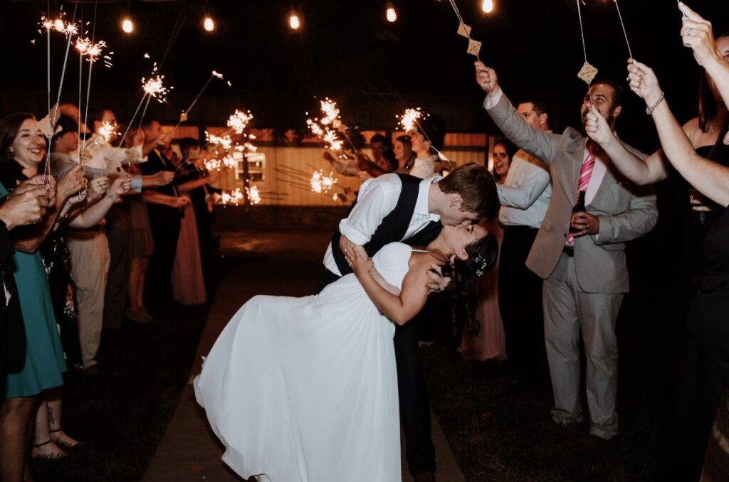 The groom dips the bride during the sparkler send off as he kisses her. 