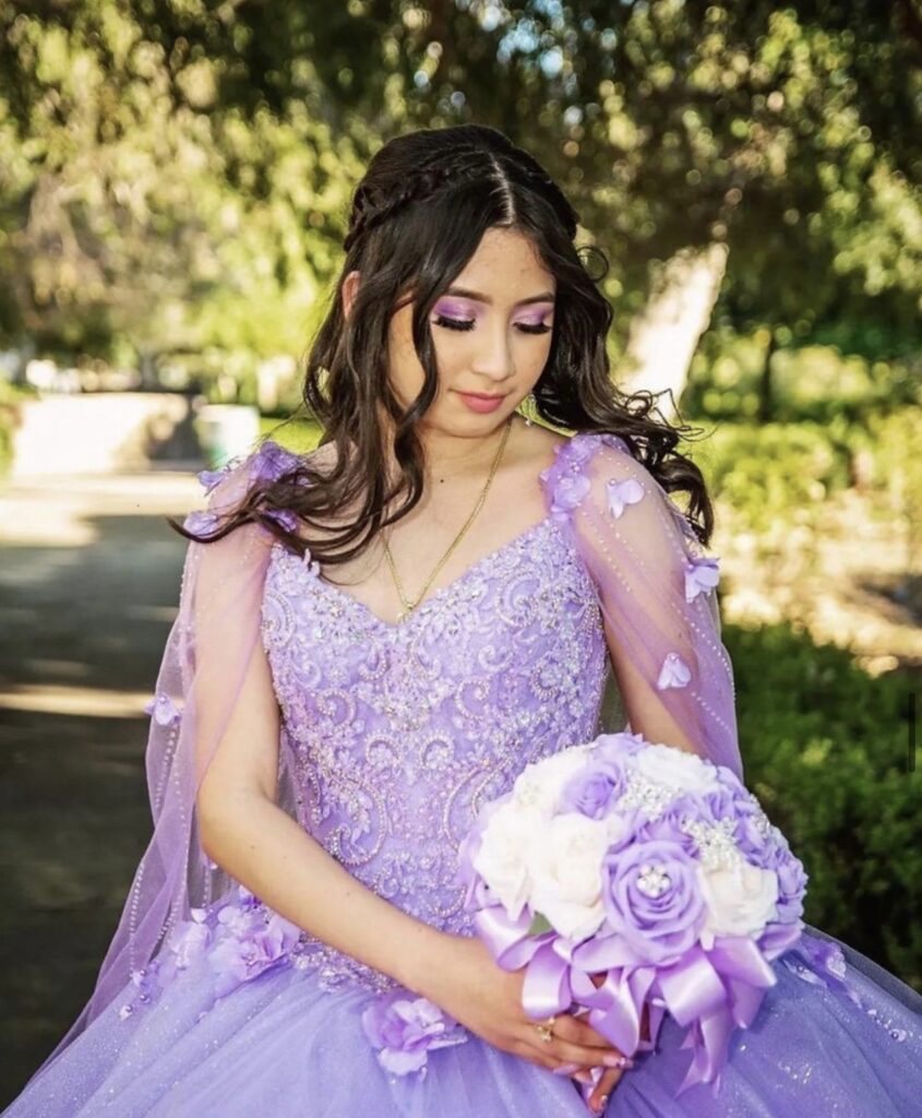 Quinceanera wearing a purple ballgown holding a white and purple bouquet wearing purple eyeshadow. 