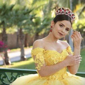 Quinceanera wearing a yellow ballgown and red ruby tiara smiling at the camera.
