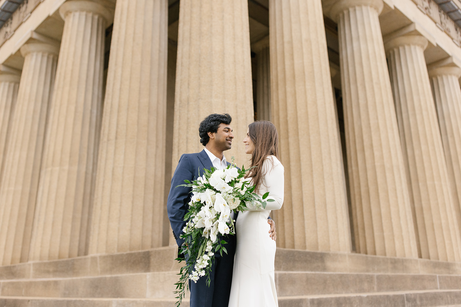 Bride and groom embrace in front of  The Parthenon in Nashville, Tennessee. The bride has a cascading bouquet of orchids.